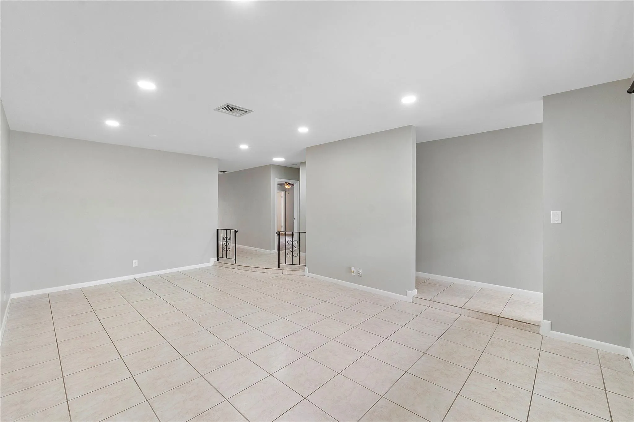Spacious room featuring tile flooring, neutral wall tones, recessed lighting, and a partial decorative railing