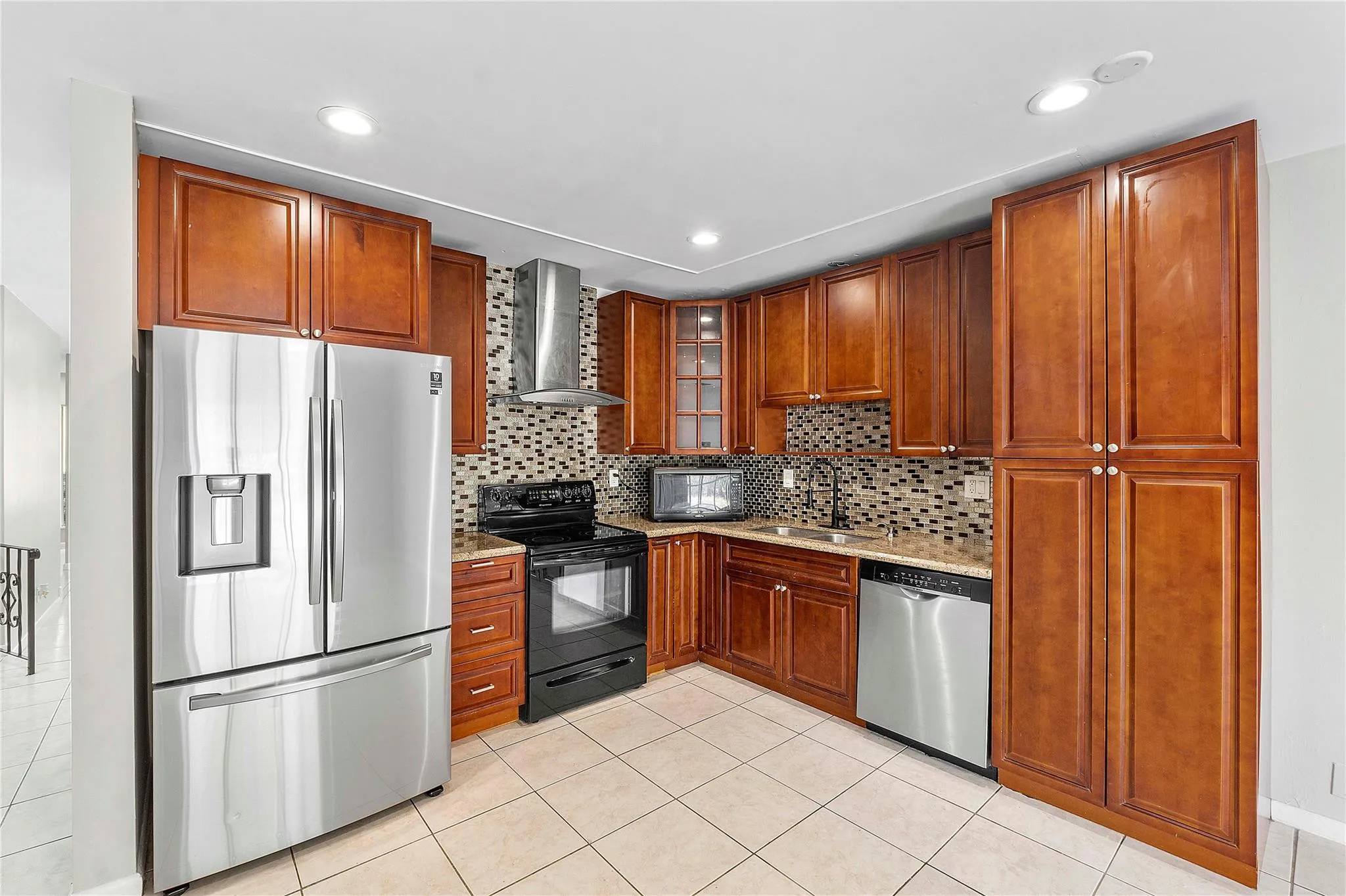 Kitchen featuring wood-finish cabinetry, stainless steel appliances, mosaic tile backsplash, stone countertops, and recessed lighting