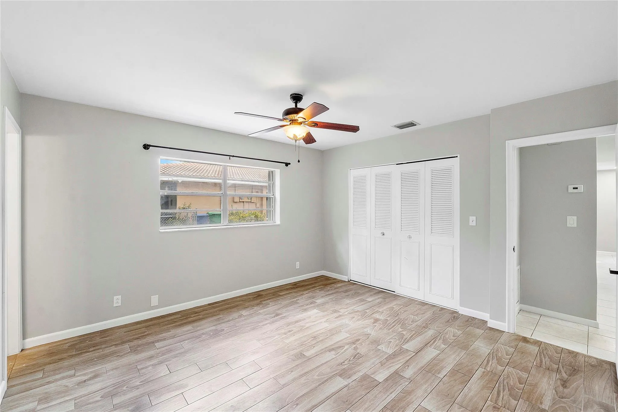 Spacious room with wood-finish flooring, light grey walls, and a ceiling fan with integrated lighting