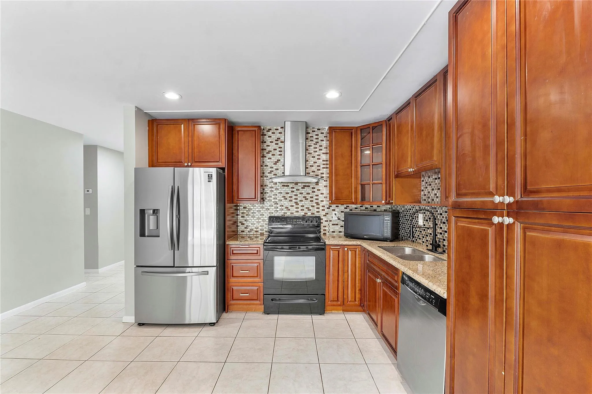 Kitchen featuring wood-finish cabinetry, granite-style countertops, stainless steel appliances, a mosaic tile backsplash, and recessed lighting