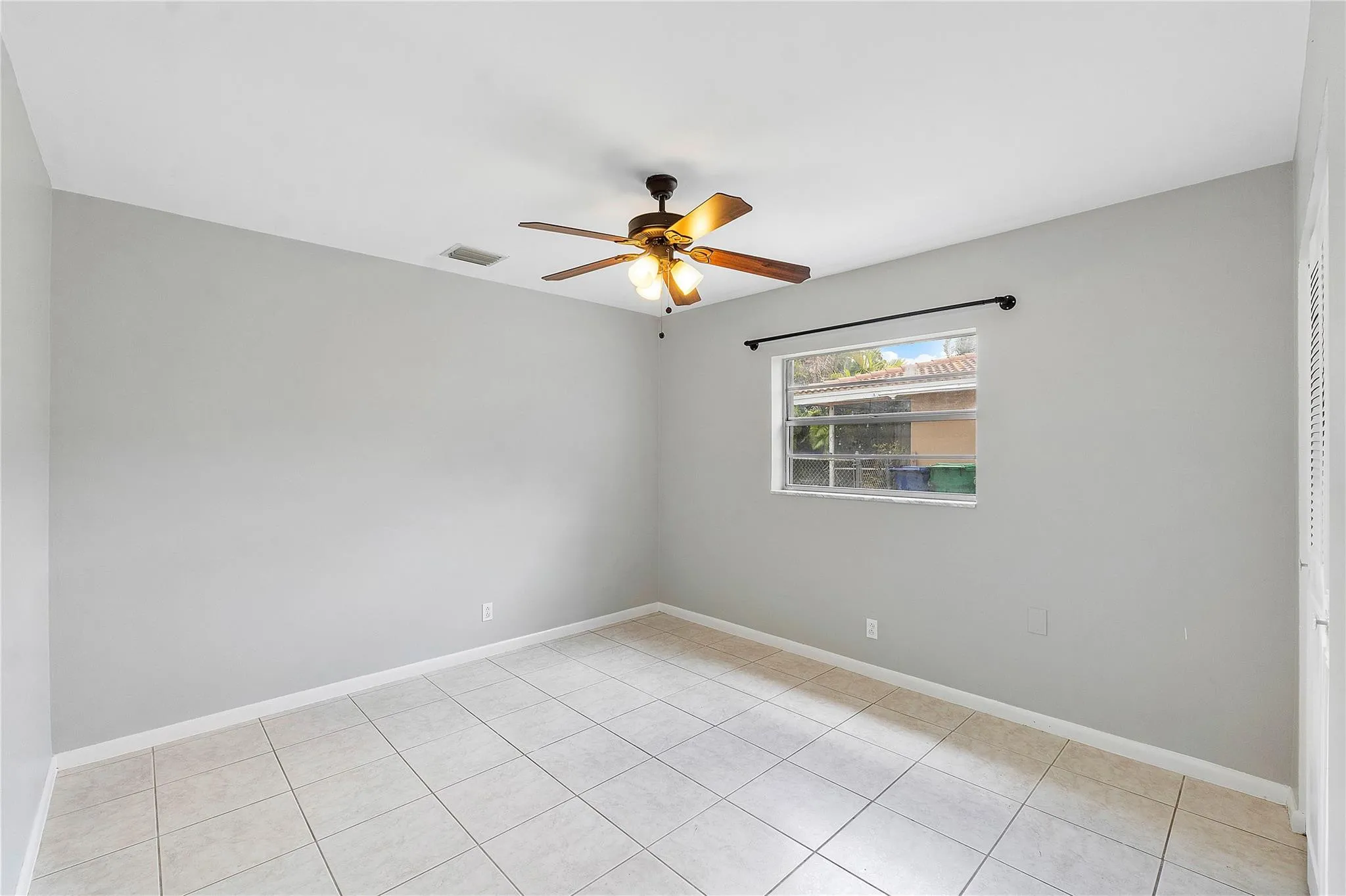 Neutral-toned interior room featuring tile flooring, a window with exterior views, and a ceiling fan