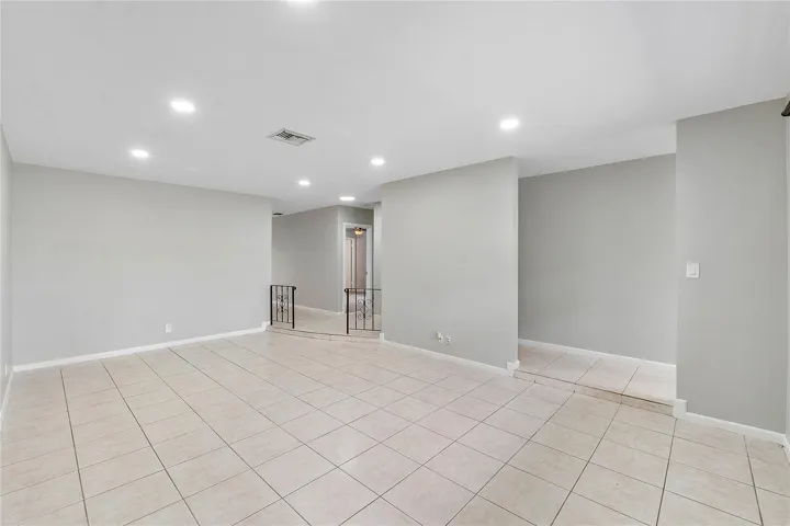 Spacious room featuring tile flooring, neutral wall tones, recessed lighting, and a partial decorative railing