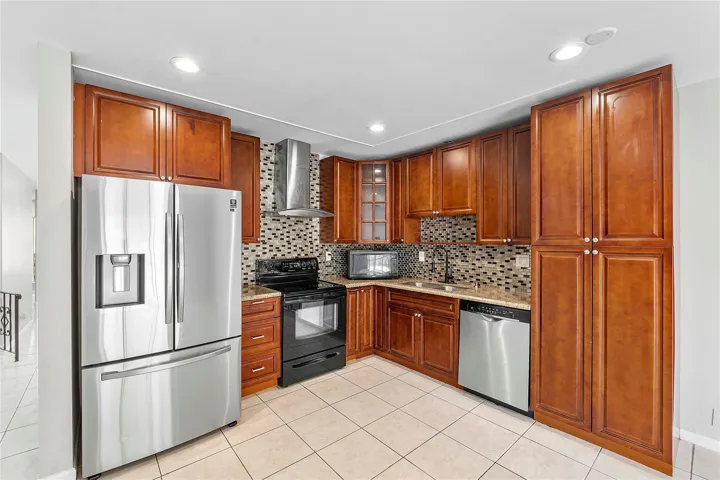 Kitchen featuring wood-finish cabinetry, stainless steel appliances, mosaic tile backsplash, stone countertops, and recessed lighting