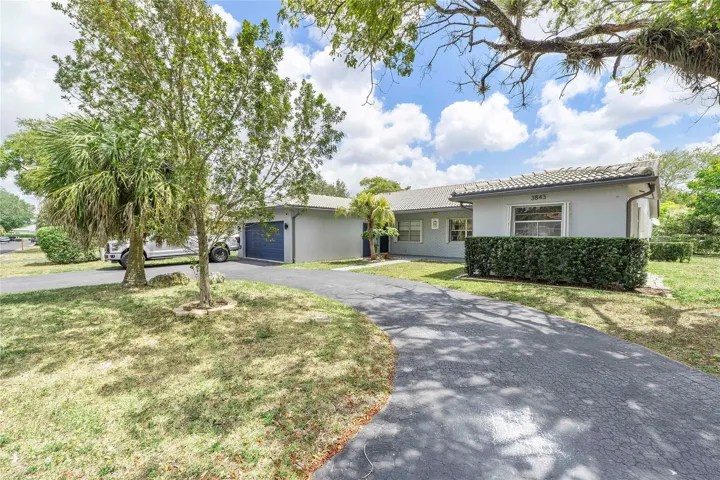 Contemporary stucco exterior with a tiled roof, mature tropical landscaping, a paved driveway, and an attached garage with a blue door