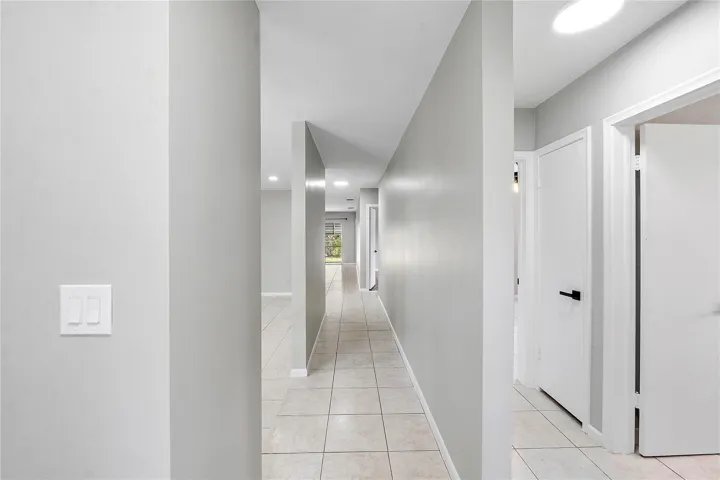 Hallway featuring neutral-toned walls, tile flooring, recessed lighting, and white interior doors with contemporary black hardware