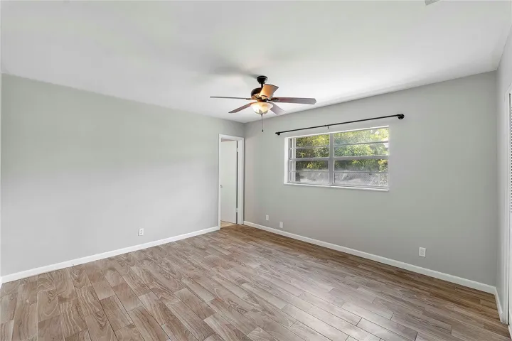 Spacious room featuring light wood-finish flooring, a ceiling fan, a large window, light gray wall paint, and white trim
