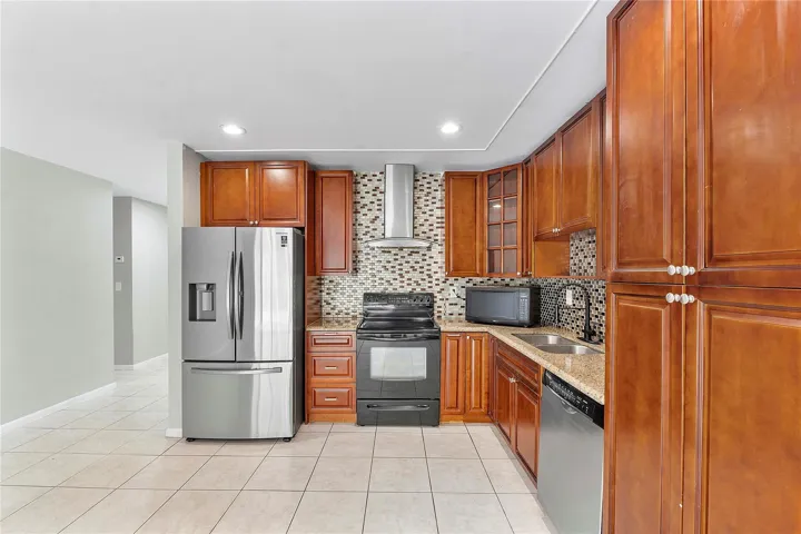Kitchen featuring wood-finish cabinetry, granite-style countertops, stainless steel appliances, a mosaic tile backsplash, and recessed lighting