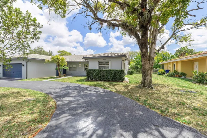 Gray stucco exterior with a tiled roof, featuring an attached garage with a dark blue door and a paved driveway