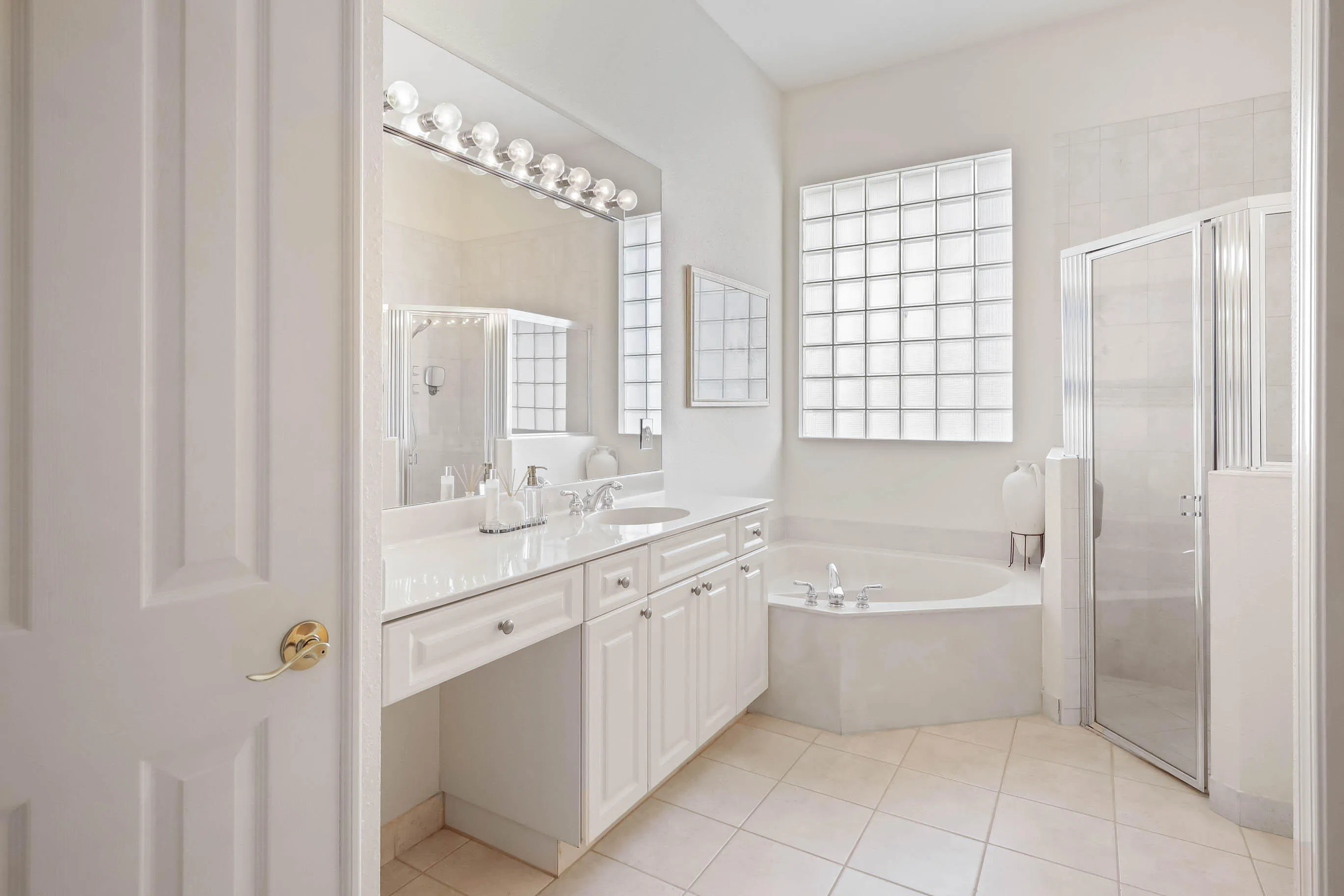 Bathroom featuring a double vanity with white cabinetry and integrated sinks, a corner soaking tub with deck-mounted fixtures, and a glass-enclosed shower