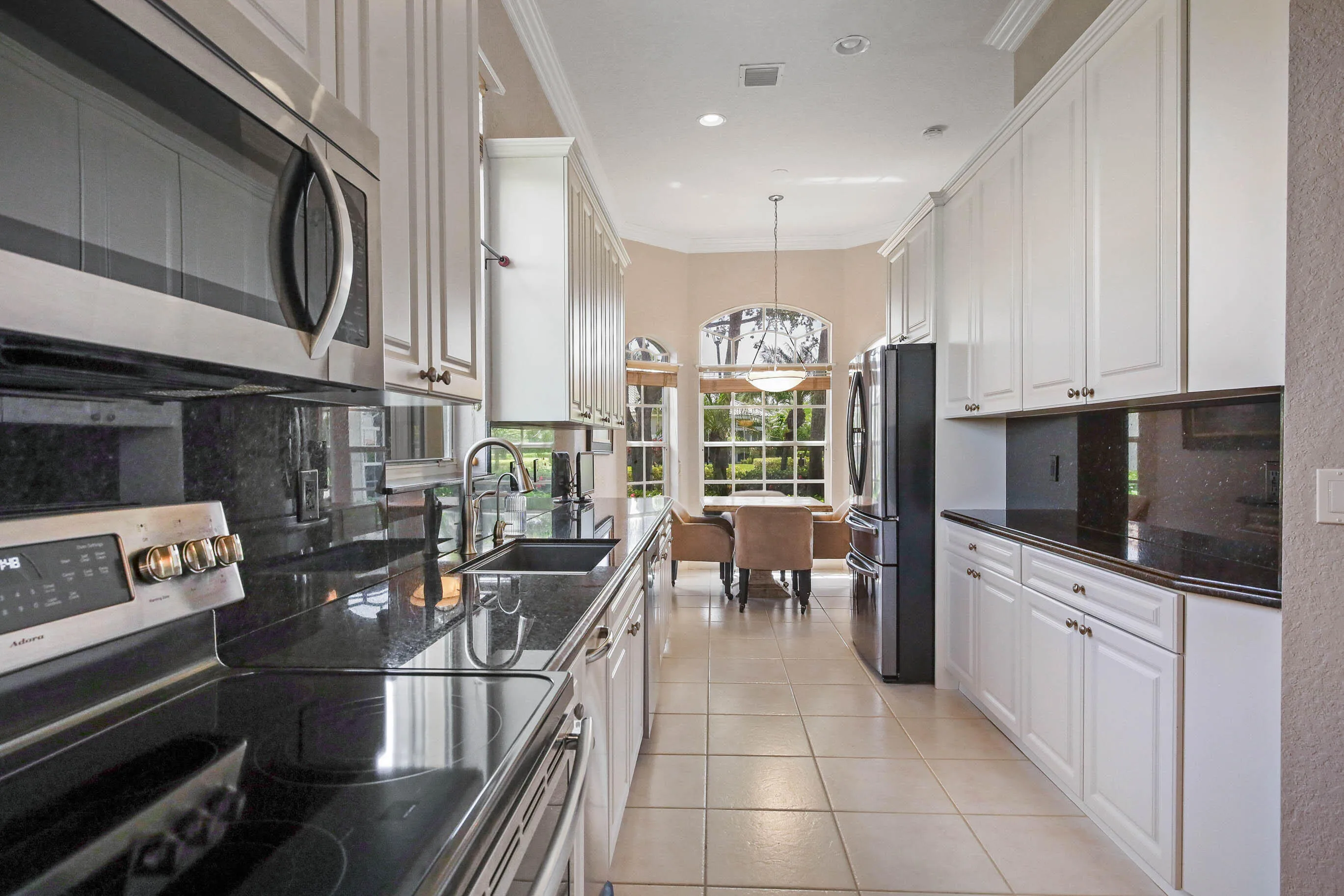 Galley kitchen featuring white cabinetry, dark stone countertops, stainless steel appliances, and tile flooring