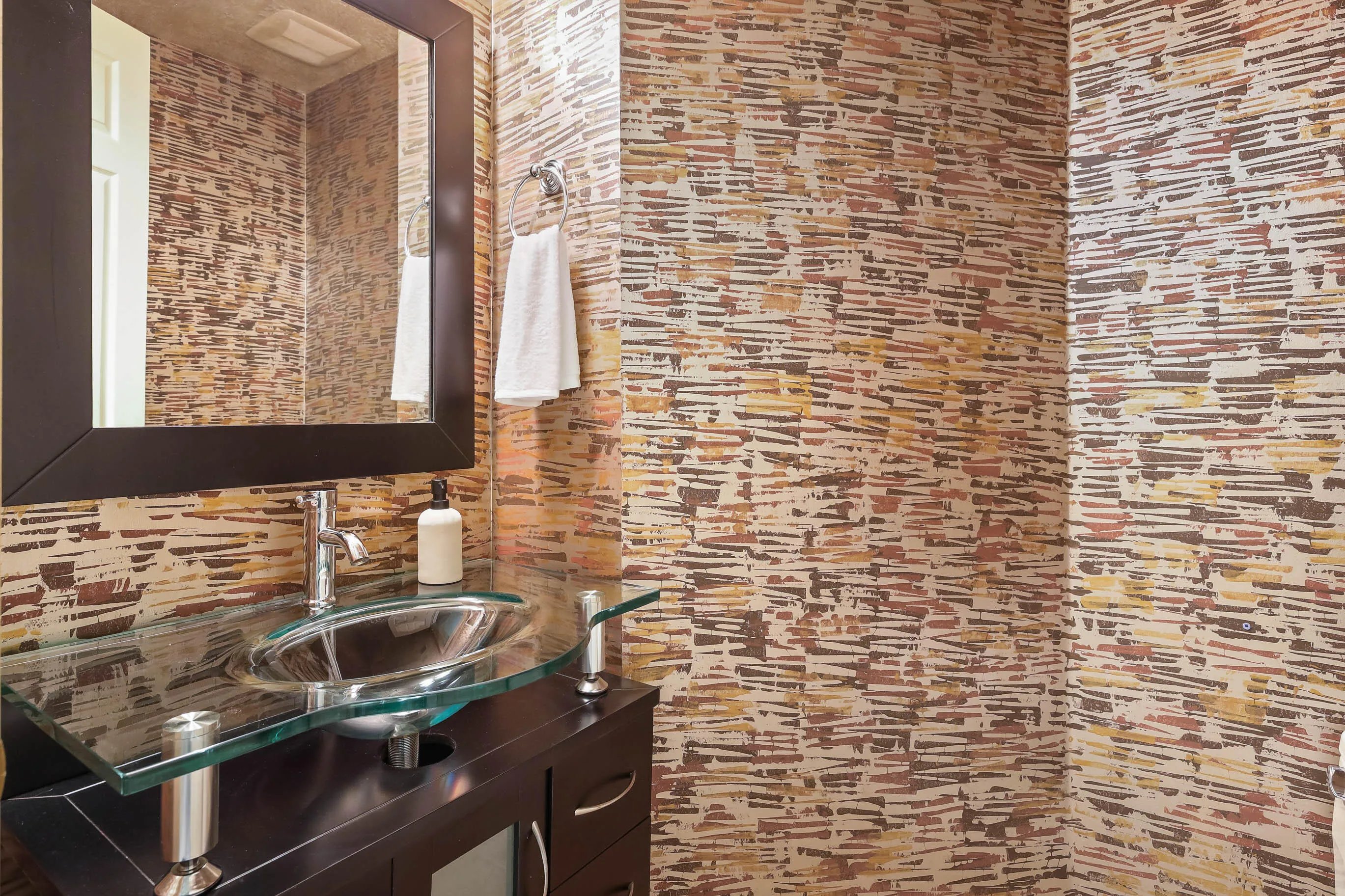 Modern vanity featuring a glass countertop and vessel sink, set against textured wallpaper