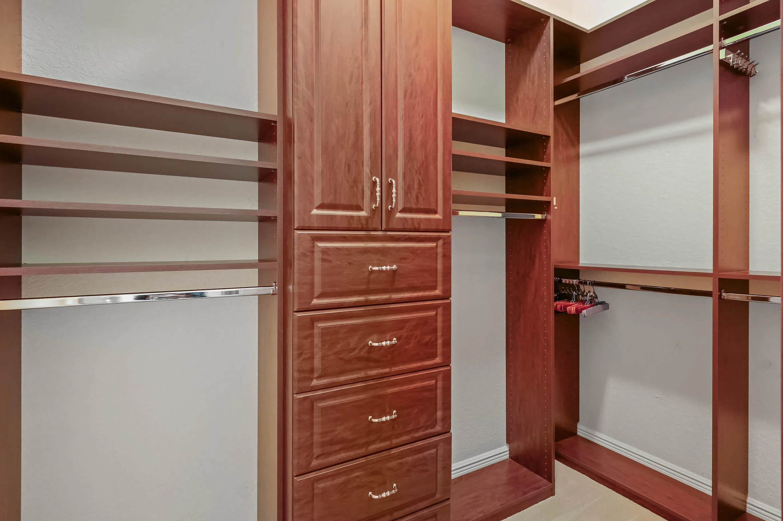 Custom closet system featuring rich wood-finish cabinetry, built-in shelving, multiple hanging rods, and integrated drawers with decorative hardware
