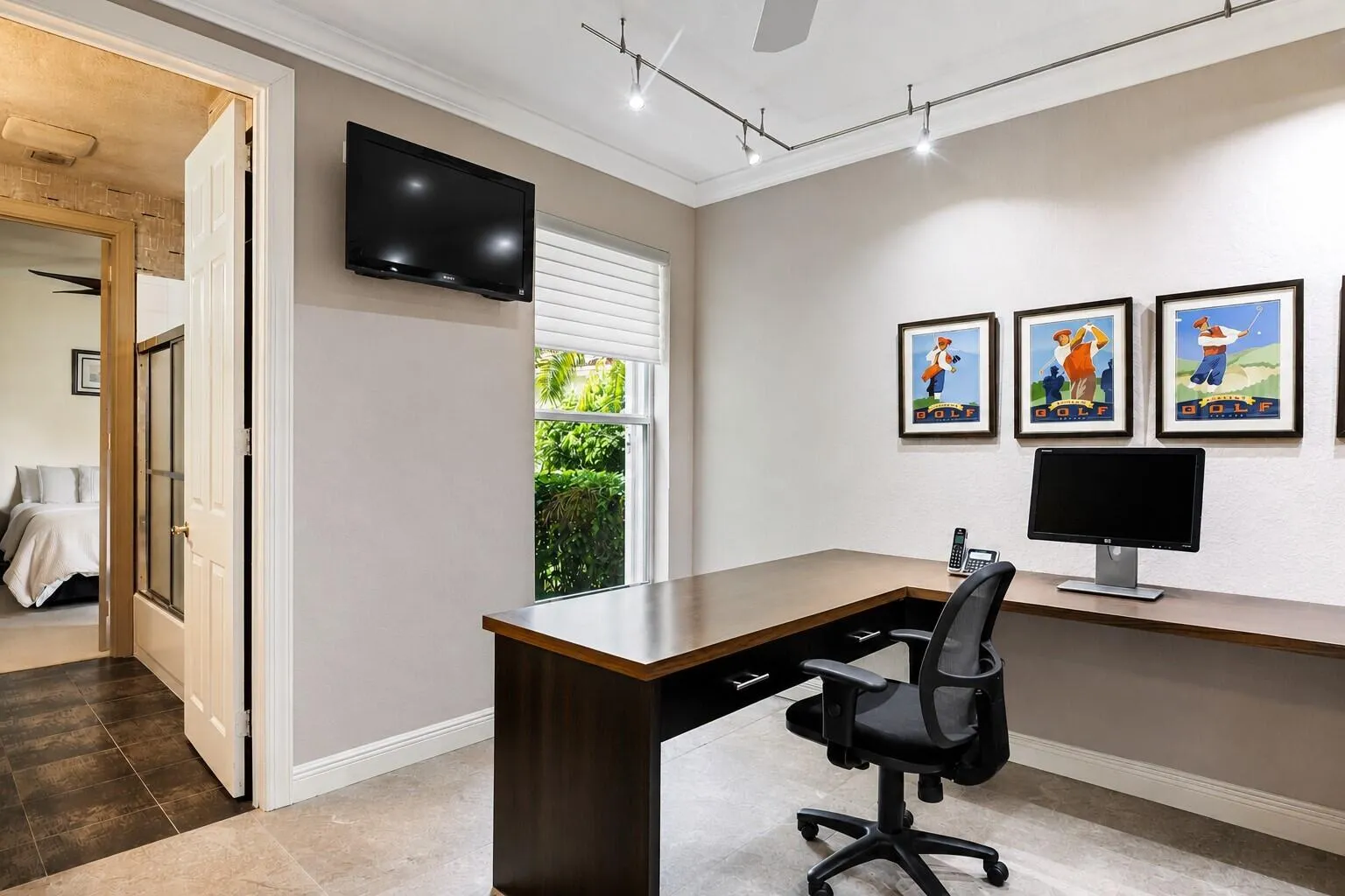 Dedicated office space featuring a built-in L-shaped desk, wall-mounted television, and track lighting