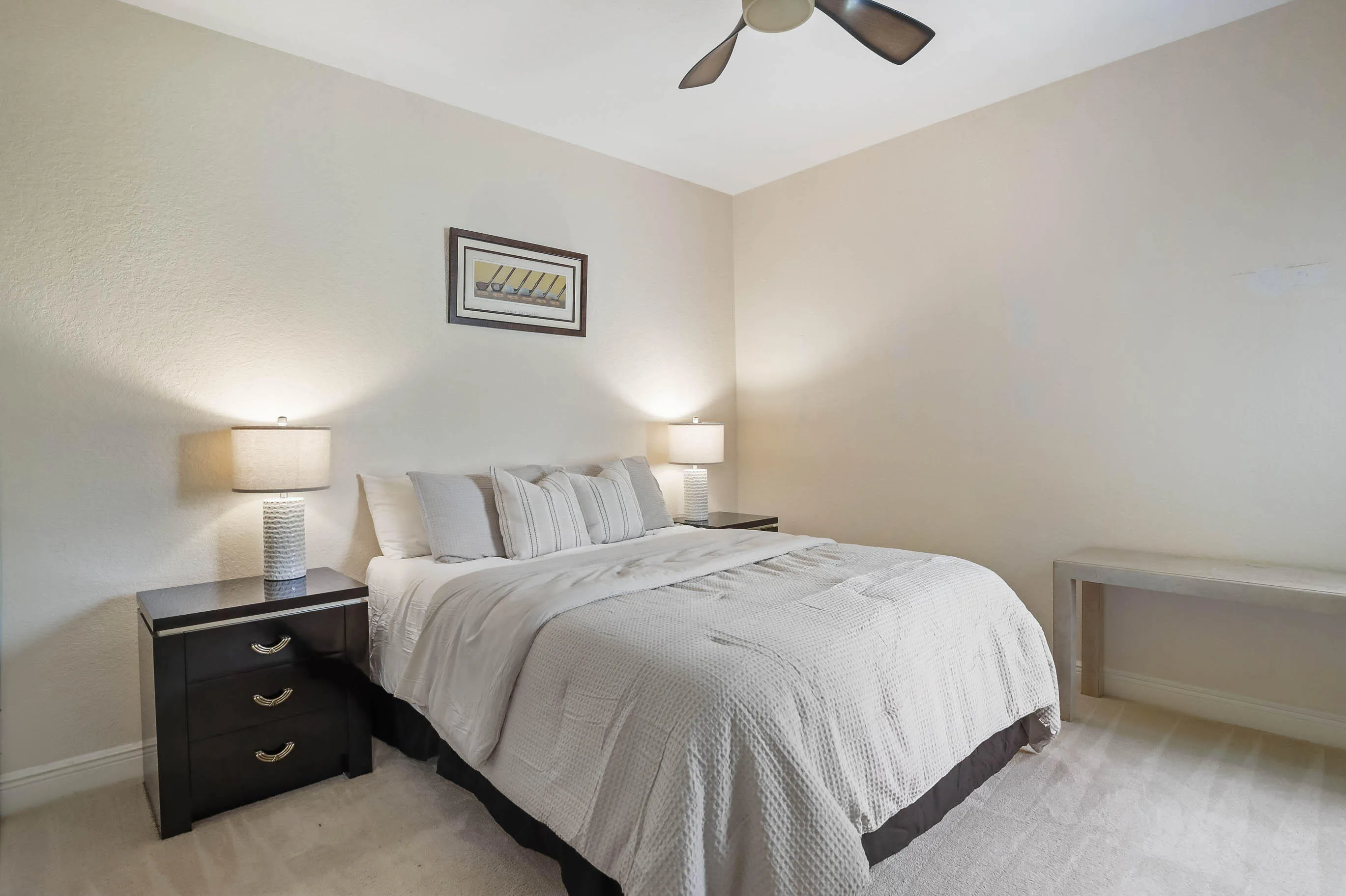 Neutral wall tones with textured finish, light-colored carpet flooring, and a ceiling fan with dark-toned blades