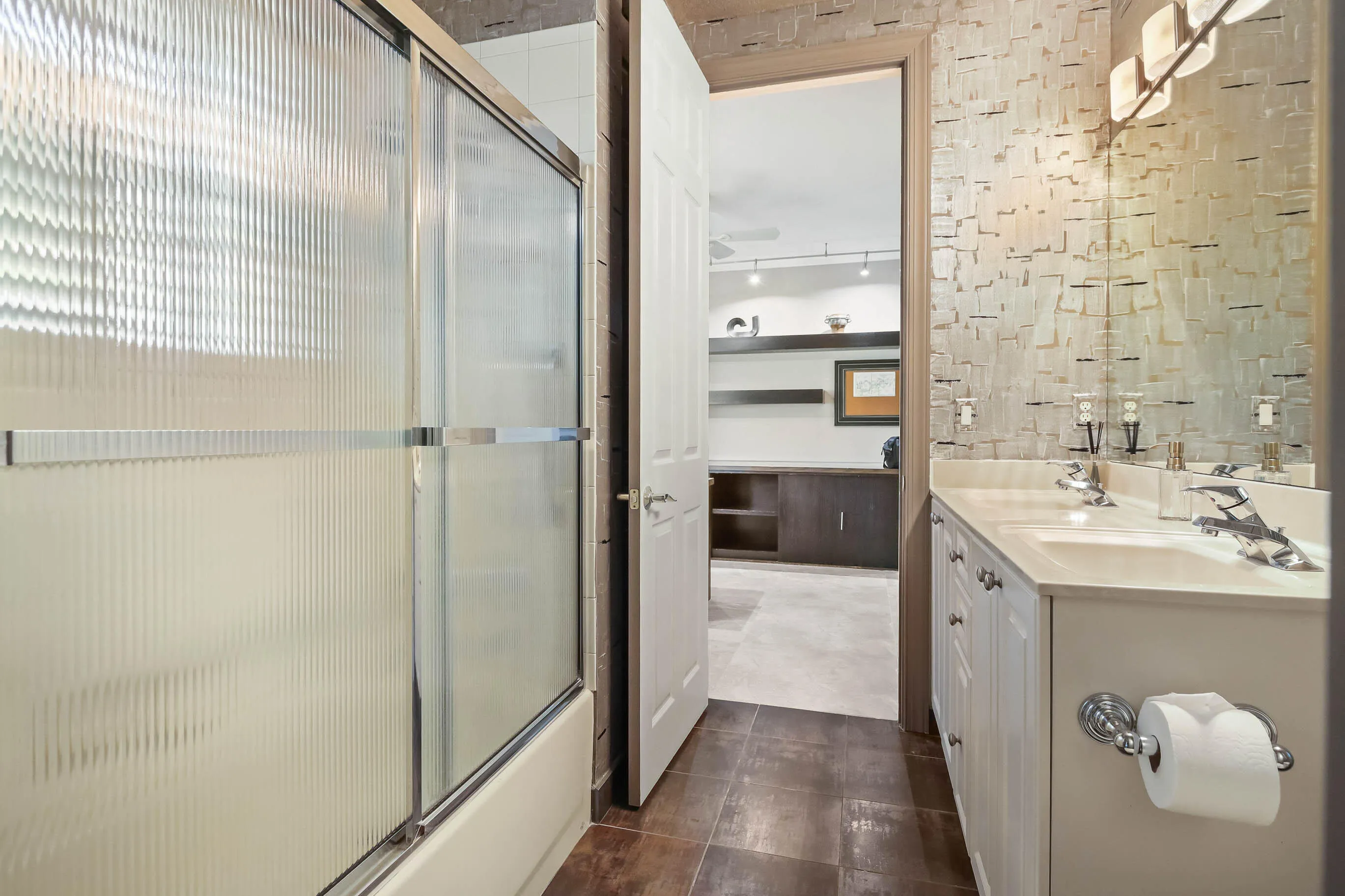 Bathroom featuring a glass shower enclosure, a dual-sink vanity with white cabinetry, a large wall-mounted mirror, modern wall sconces, and a textured wall finish