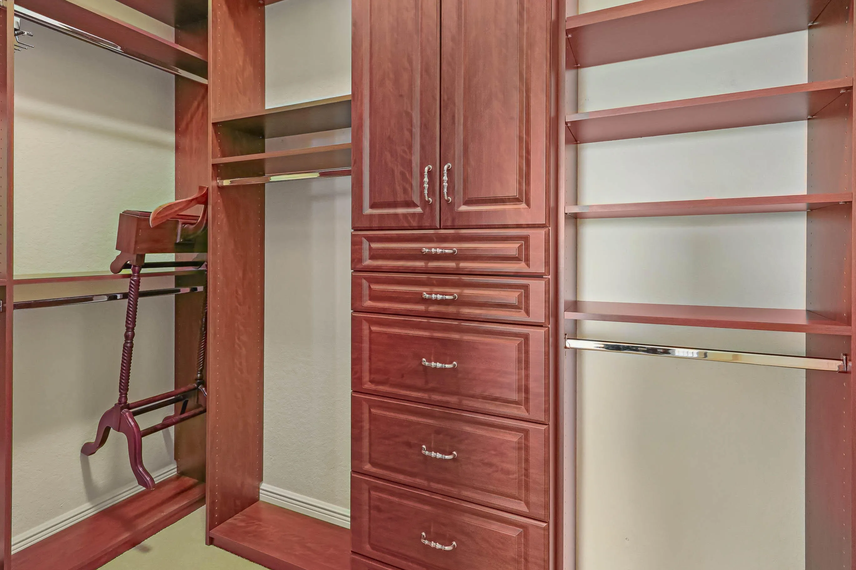 Custom closet system featuring rich wood-finish cabinetry, multiple built-in shelving units, integrated hanging rods, and an array of drawers with decorative hardware