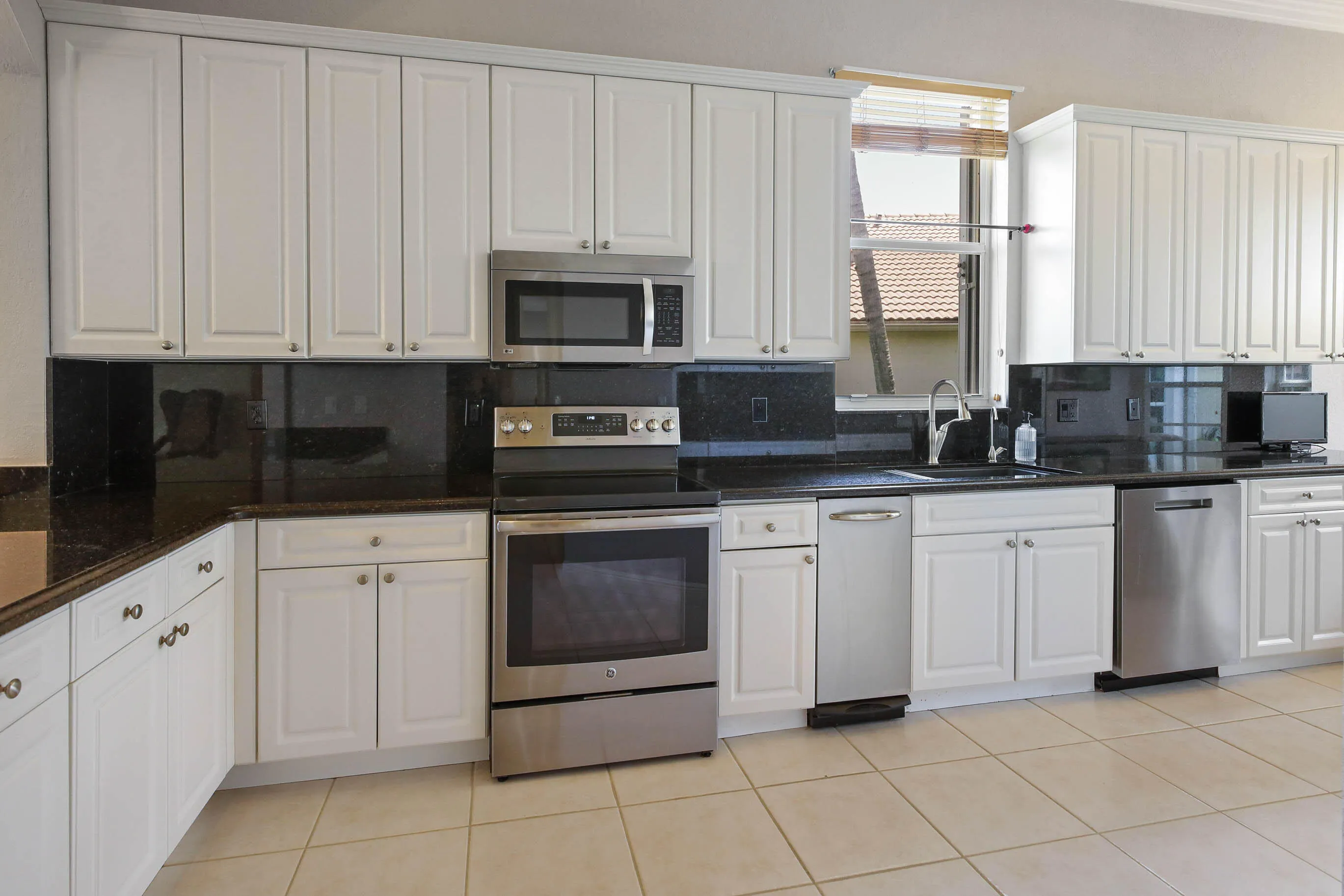 Kitchen featuring white cabinetry, dark countertops, dark backsplashes, stainless steel appliances, and tiled flooring