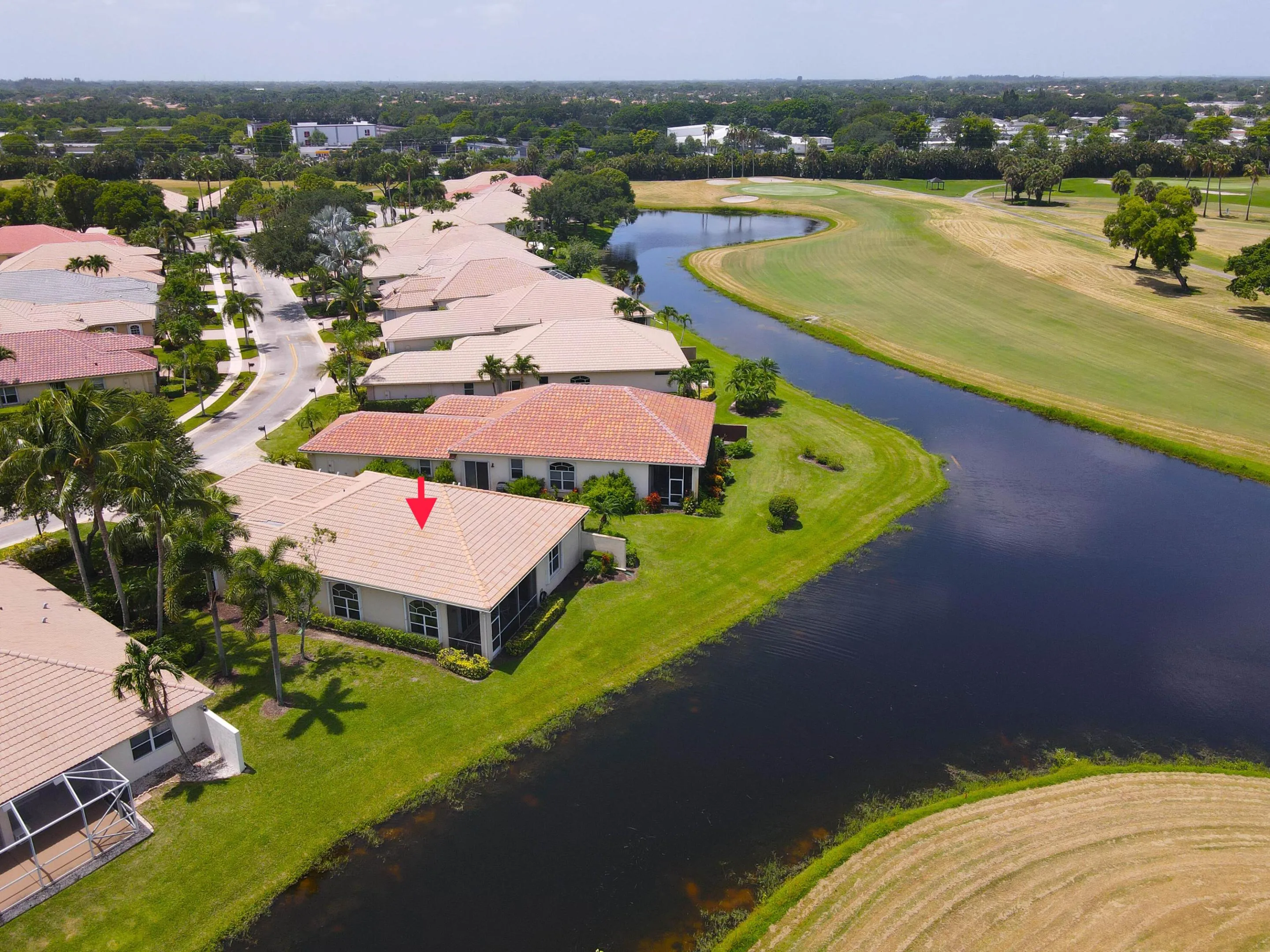 Waterfront property featuring a screened enclosure, tile roof, lush green lawn, and mature palm trees