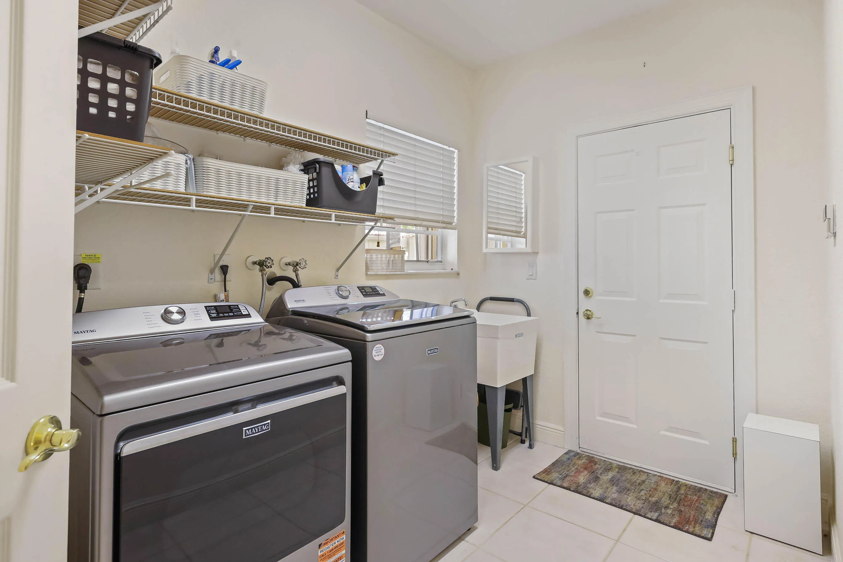 Utility room featuring a laundry sink, two appliances, upper shelving, and tile flooring