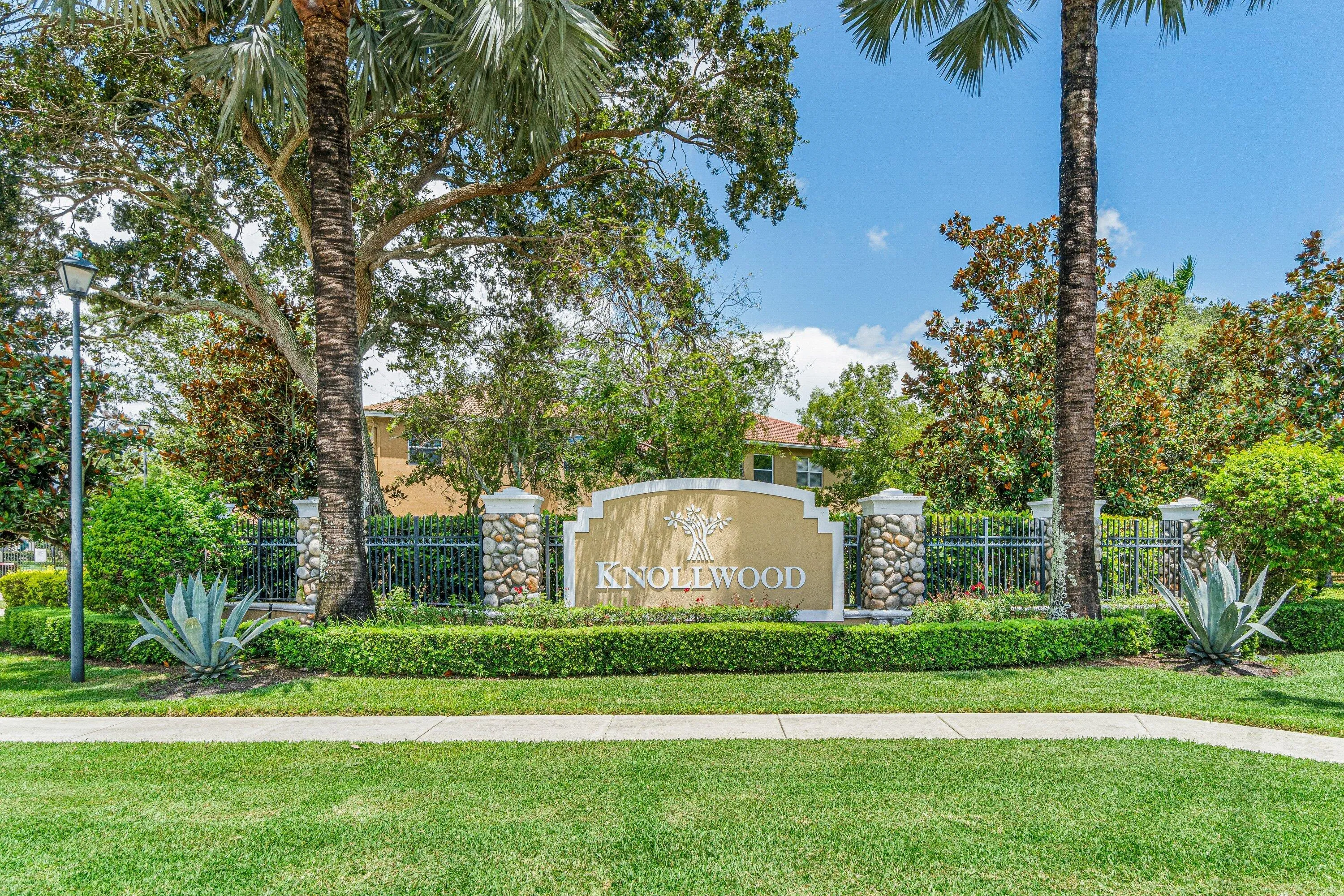 Entry monument with stone-clad pillars, wrought iron fencing, and manicured landscaping