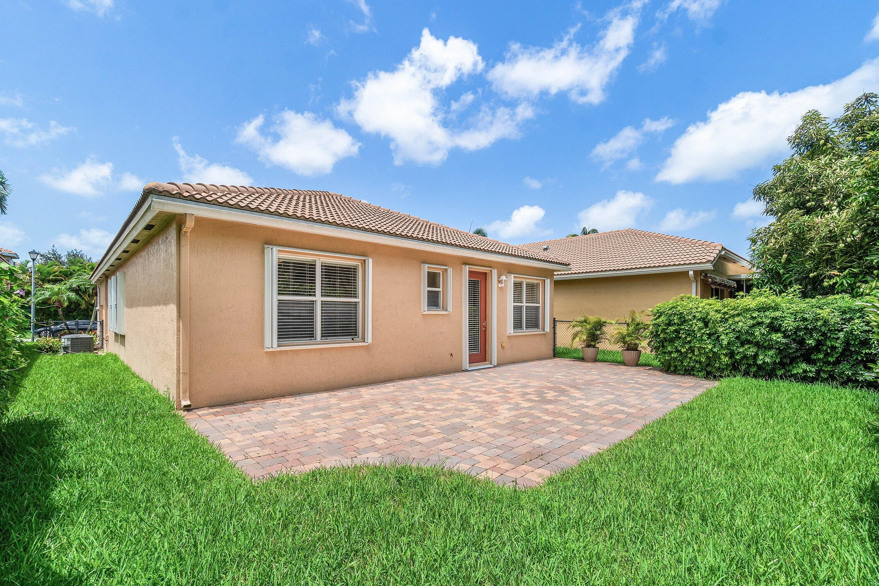 Exterior featuring a paver patio, stucco finish, tiled roof, multiple windows, and a manicured lawn