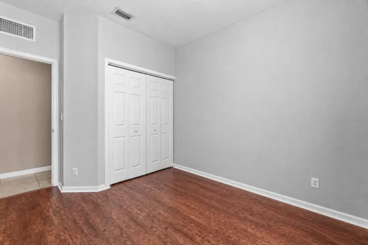 Interior room featuring luxury vinyl flooring, light gray walls, a window with horizontal blinds, and white baseboards and bifold closet office or bedroom