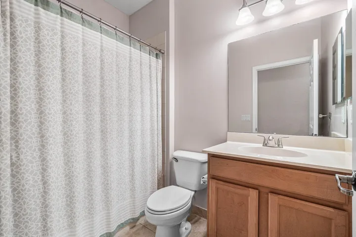 Bathroom featuring a light wood-finish vanity with a single sink, a large wall-mounted mirror, and tile flooring