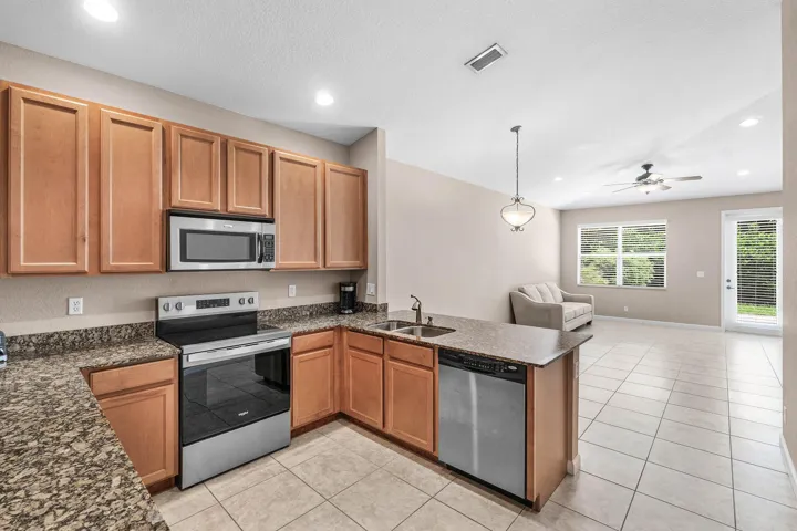 Open-concept kitchen featuring wood cabinetry, granite-finish countertops, and stainless steel appliances
