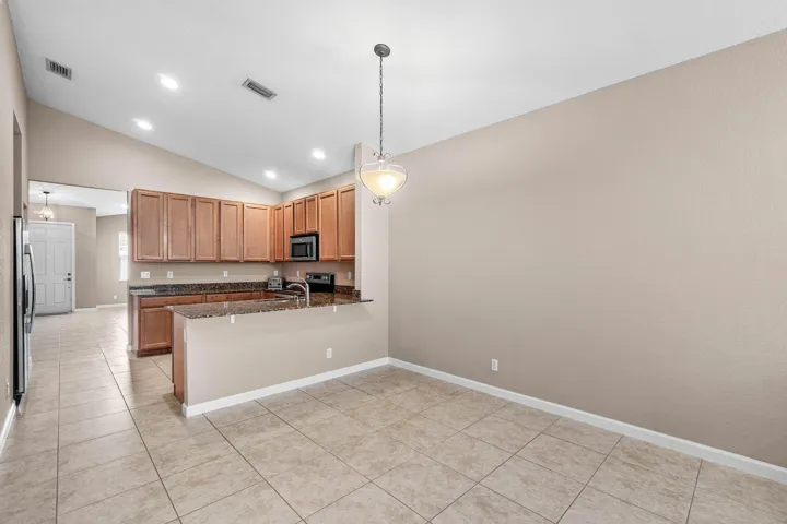 Kitchen and dining area featuring tile flooring, vaulted ceiling, recessed lighting, wood cabinetry, and a snack bar counter with a granite-finish surface