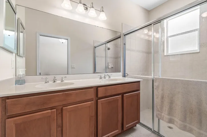 Dual sink vanity with wood-finish cabinetry, white countertop, and expansive wall-mounted mirror