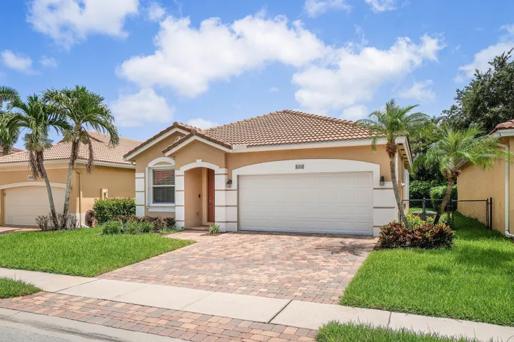 Single story residence featuring a tile roof, stucco exterior, and a paver driveway