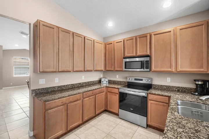 Kitchen featuring wood cabinetry, granite-style countertops, stainless steel appliances, and recessed lighting