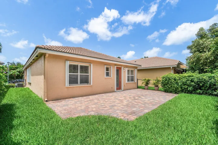 Exterior featuring a paver patio, stucco finish, tiled roof, multiple windows, and a manicured lawn