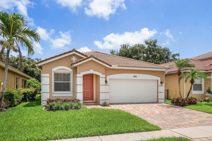 Single story residence featuring a tile roof, stucco exterior with decorative trim, and a paver driveway