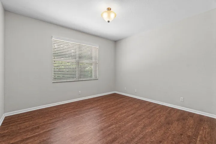 Spacious room featuring luxury vinyl flooring, light grey walls, white baseboards, a window with horizontal blinds, and a ceiling-mounted light fixture