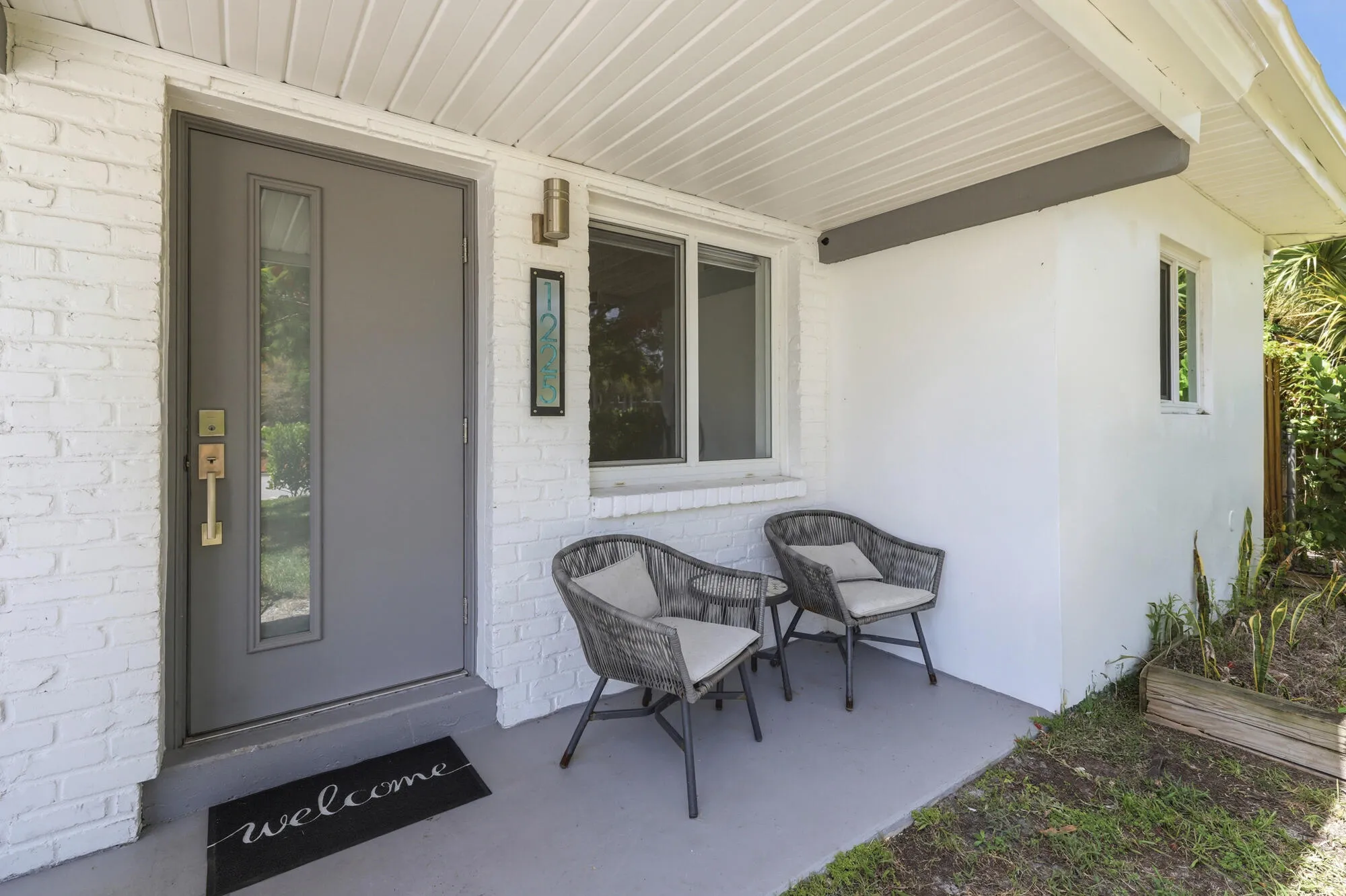 White-painted brick facade with a gray entry door featuring a vertical window panel and brass hardware