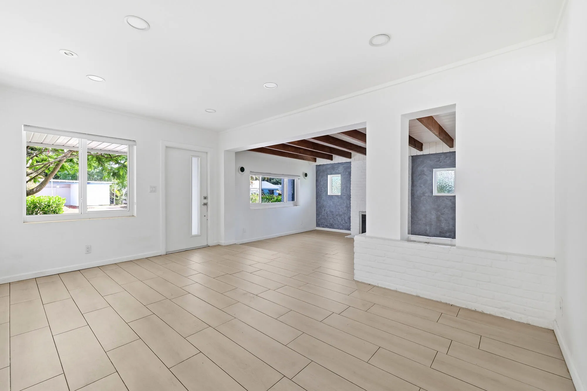 Spacious interior featuring light-toned plank tile flooring, recessed lighting, and a white entry door with a frosted glass insert