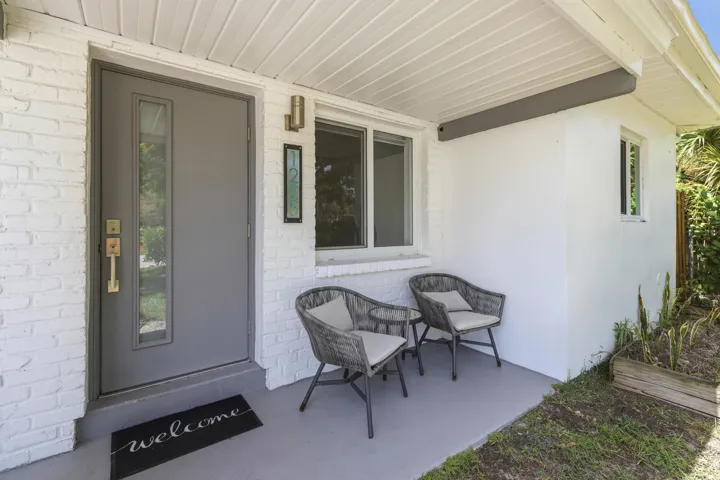 White-painted brick facade with a gray entry door featuring a vertical window panel and brass hardware