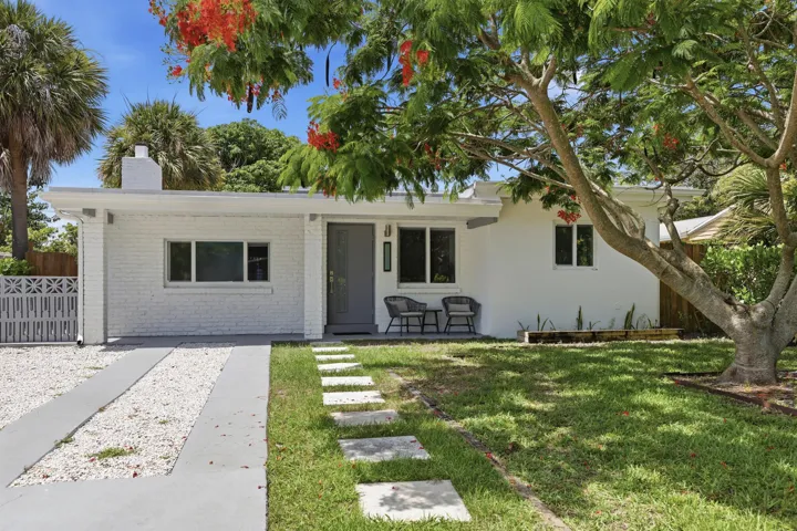 White brick and stucco exterior with a gray front door, flat roofline, and a driveway featuring concrete strips and white gravel