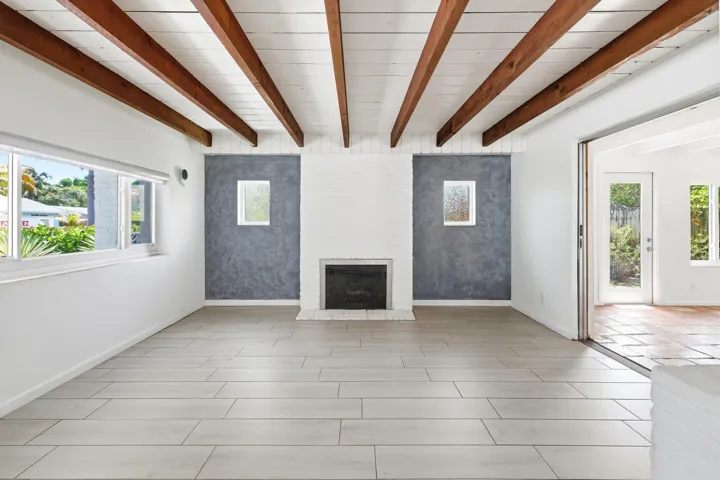 Exposed wood beams over a white plank ceiling and fire place