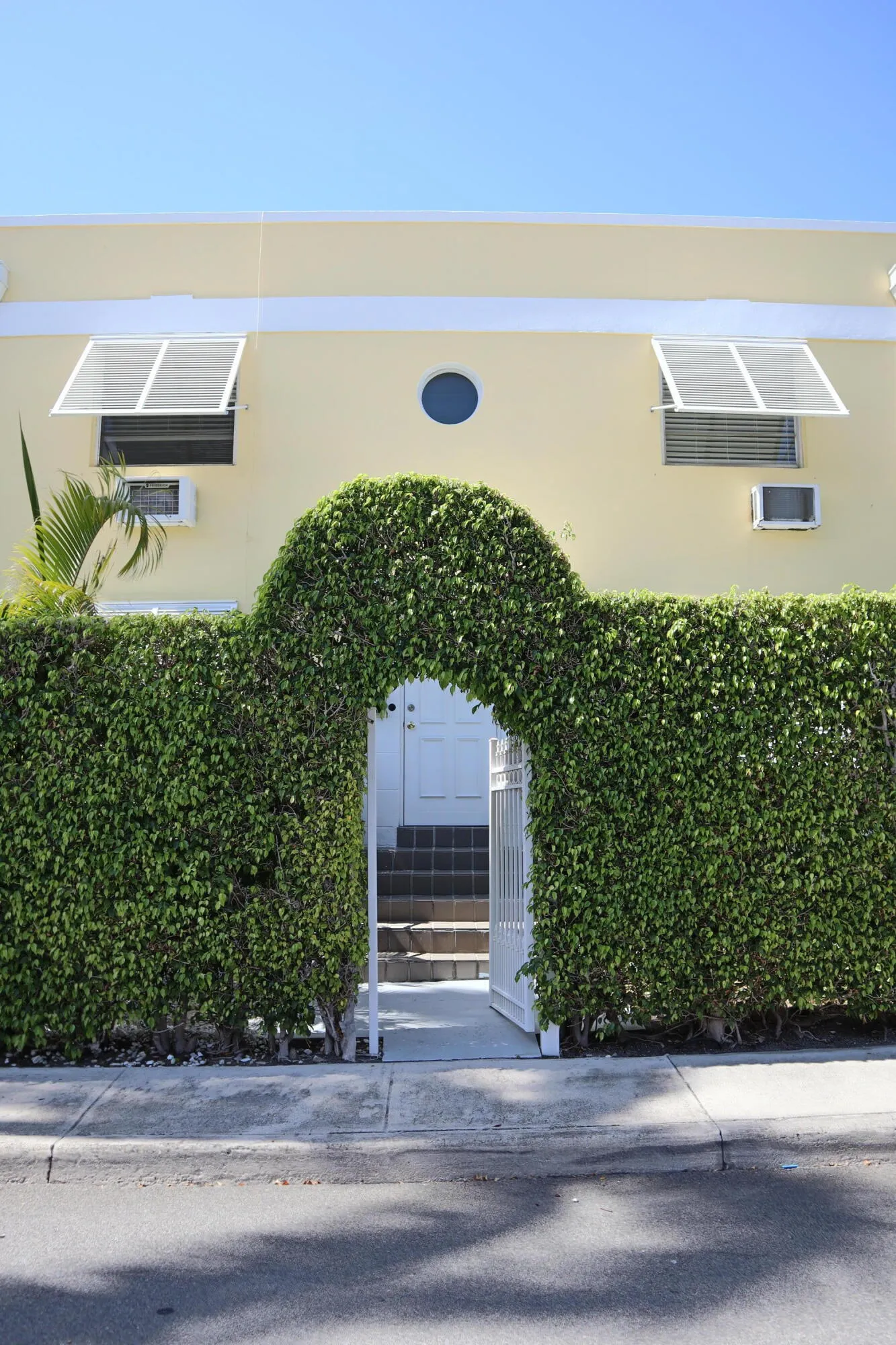 Manicured hedge with an arched entryway leading to steps and a white door