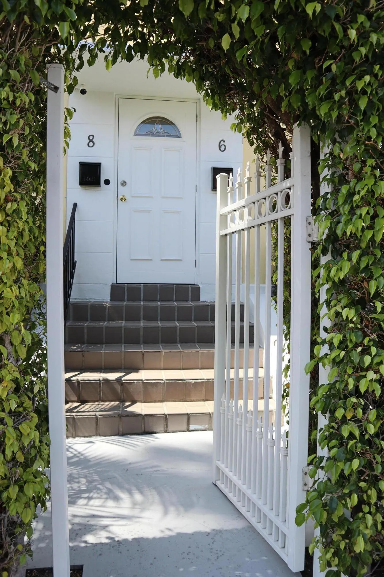 Gated entry featuring an arched, vine-covered trellis and a white metal pedestrian gate