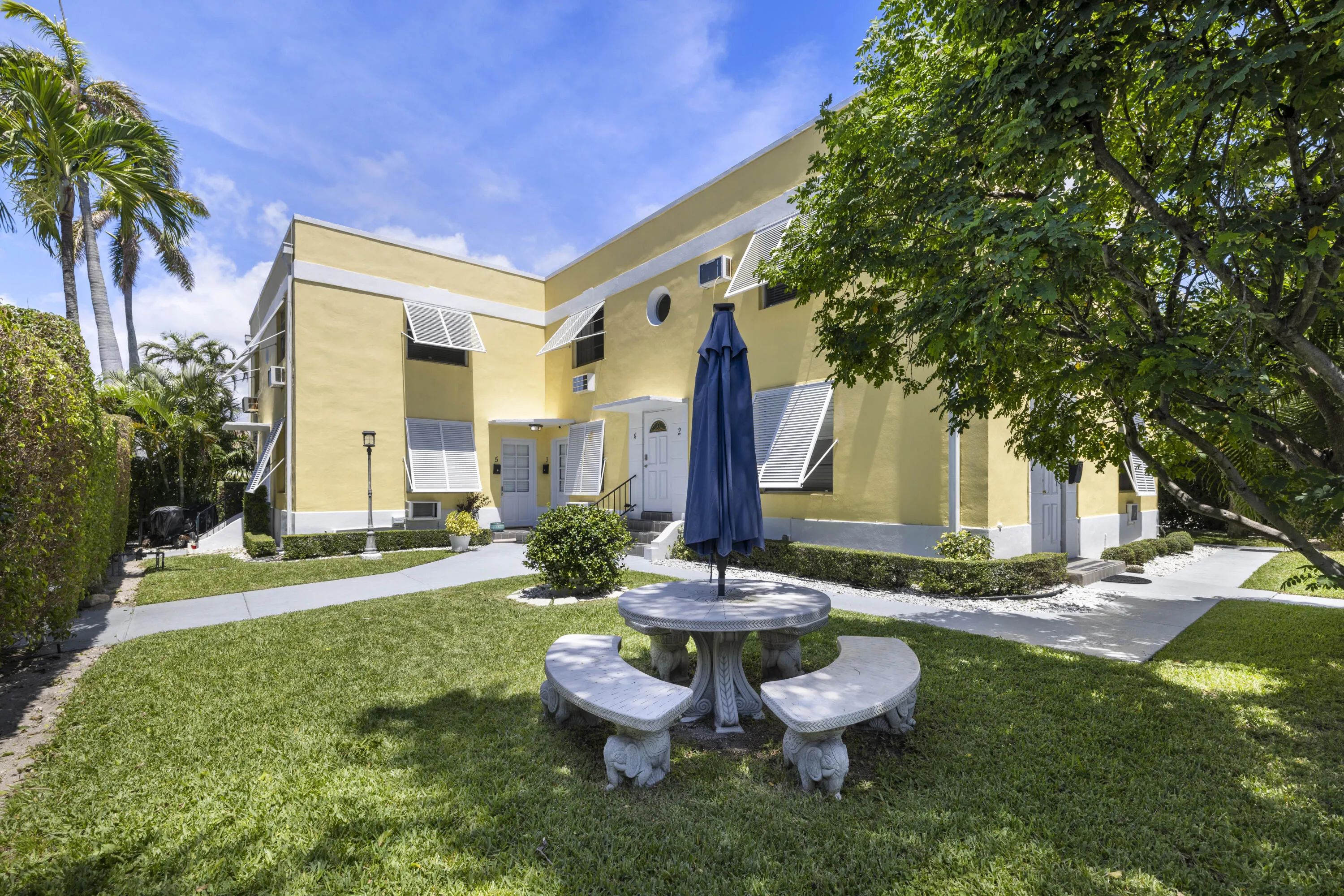 Exterior featuring a yellow facade with white trim, multiple entryways, and louvered window awnings