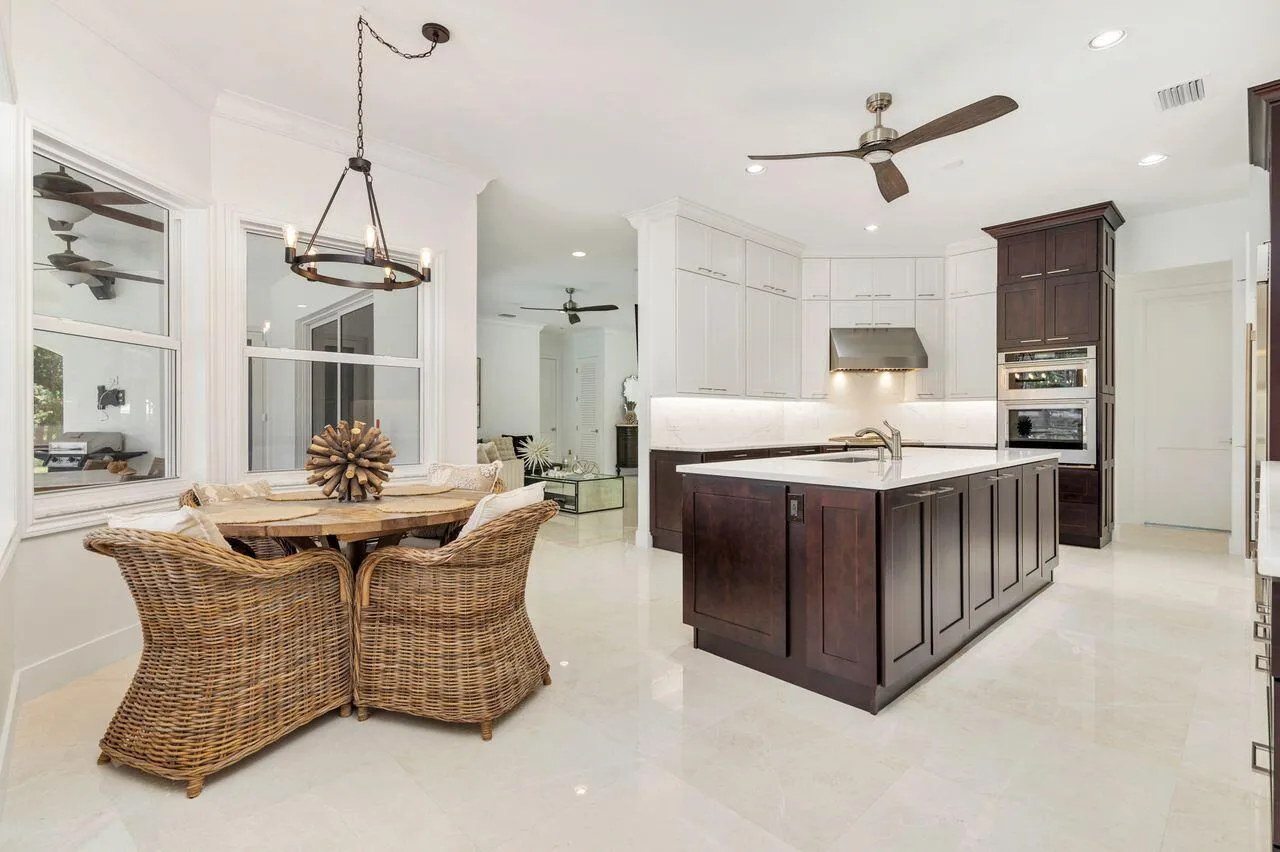 Modern kitchen featuring a large central island with a sink, white upper cabinetry, rich dark wood lower cabinetry, and built-in stainless steel appliances including a wall oven and microwave
