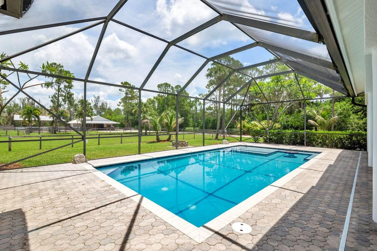Screened-in outdoor living space featuring a geometric swimming pool with integrated spa, paver patio, and a backdrop of mature trees