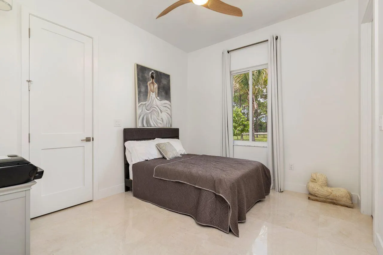 Light-filled guest bedroom featuring marble flooring, a modern ceiling fan, and a large window with outdoor landscaping visible