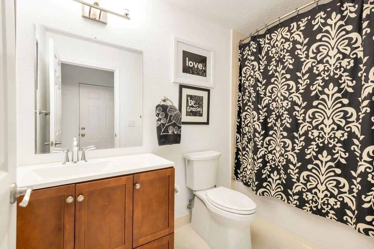 Bathroom featuring a wood-finish vanity with a white countertop and integrated sink, brushed nickel faucet, wall-mounted mirror, and overhead vanity lighting