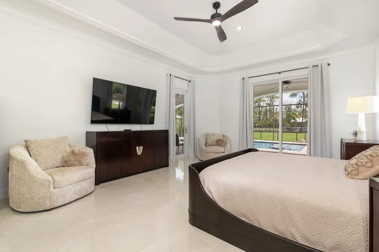 Spacious room featuring marble flooring, a tray ceiling with a dark-toned ceiling fan, and sliding glass doors opening to an exterior patio and pool area