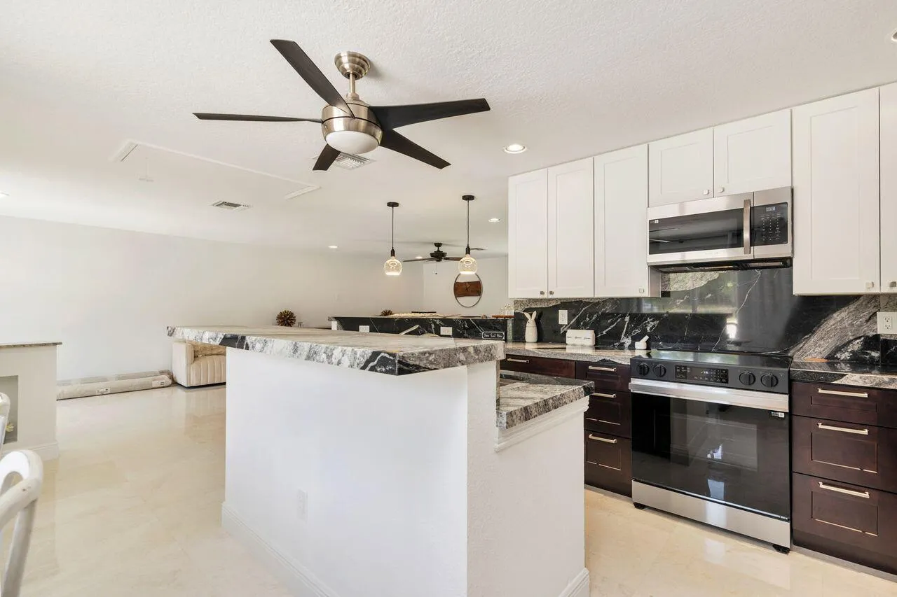Kitchen featuring white upper cabinetry, dark lower cabinetry, stainless steel appliances, and contrasting countertops with backsplash