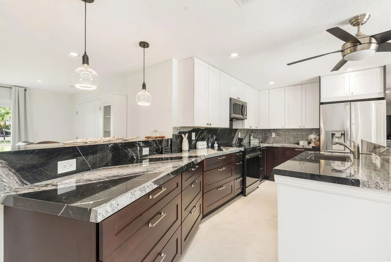 Gourmet kitchen featuring dark wood cabinetry, white upper cabinets, stainless steel appliances, and contrasting dark countertops with a white vein pattern